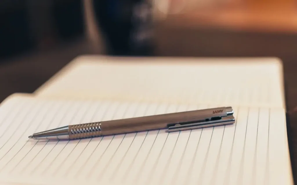 Open notebook with pen on a table, mug in background, cozy s